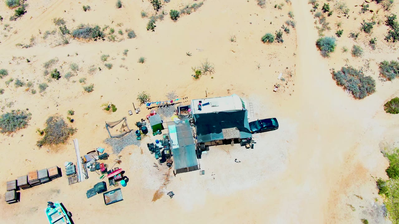 Aerial view of desert scrub around a camp with trailer, car, shade, and equipment.