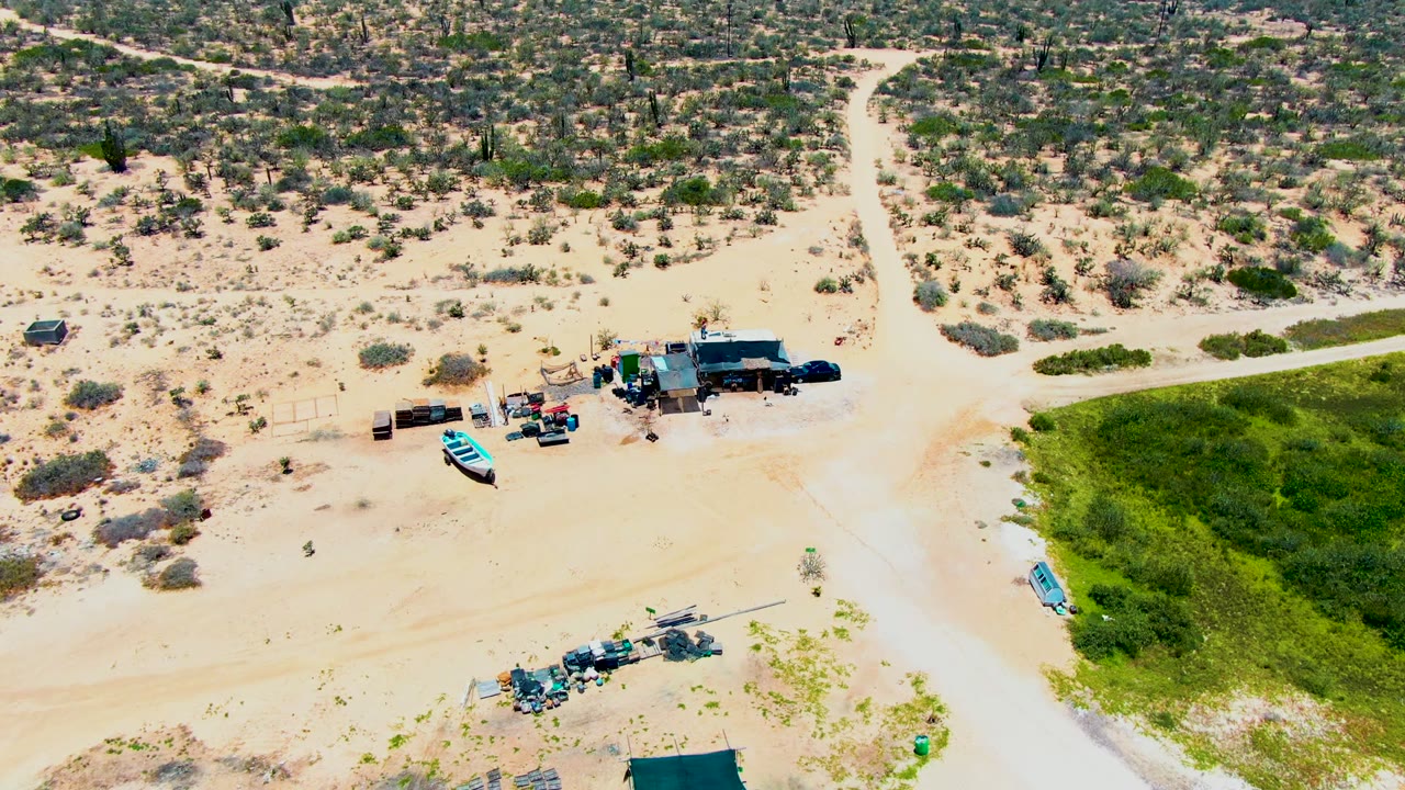 Aerial view of a blue boat near a small structure and dirt tracks in scrubby desert.