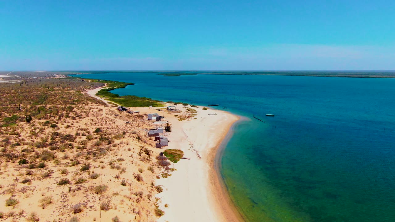 Aerial coastline with huts between desert scrub and clear blue water.