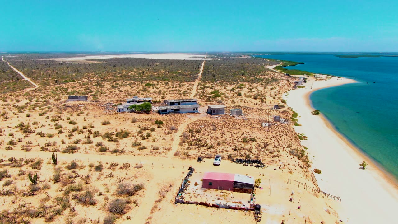 Drone view of a white car near scattered buildings and a curved beach.