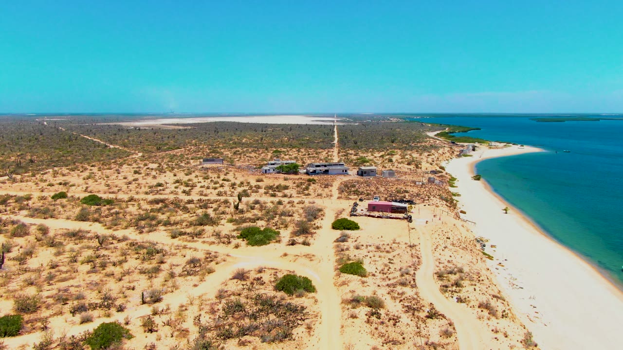 High aerial view of sandy desert, beach buildings, shoreline, and turquoise water.