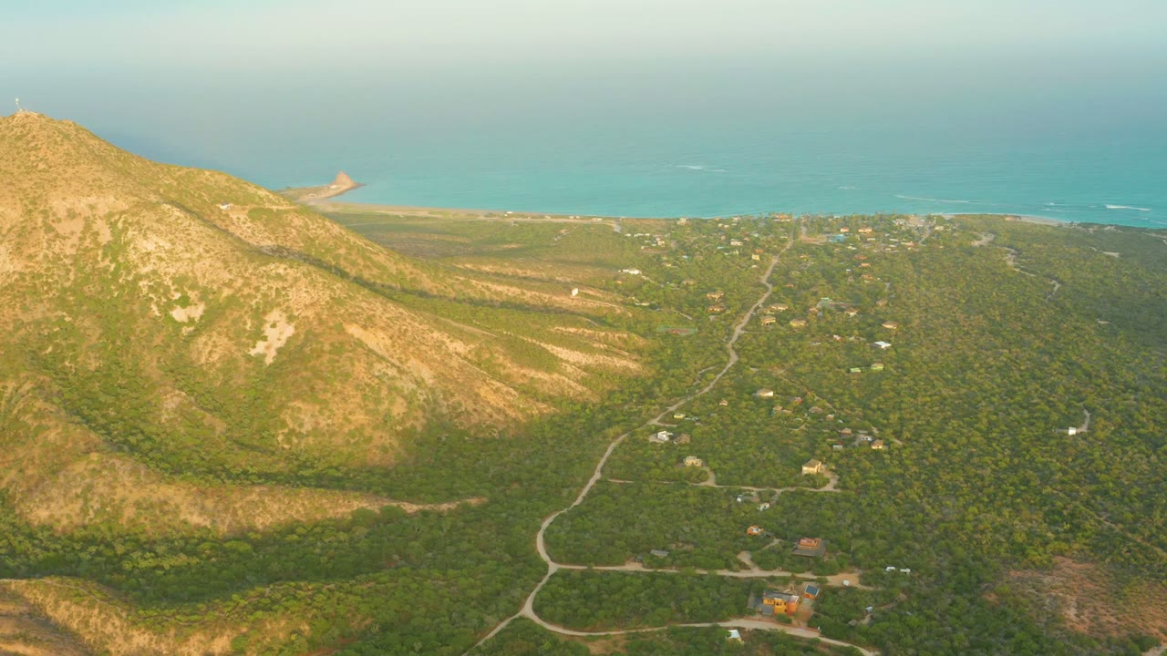 Rocky mountain slope beside green terrain with roads and ocean in the distance.