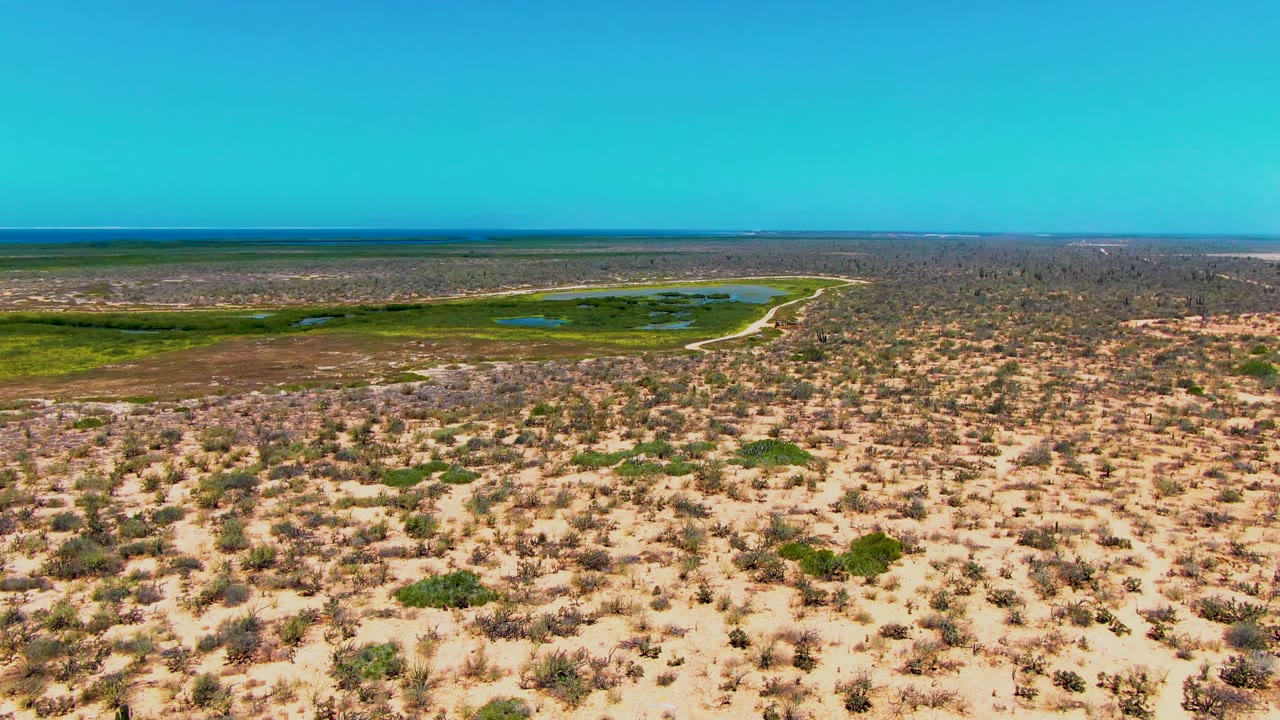At two seconds, the frame shows San Carlos desert scrub stretching toward green patches and small ponds under a clear blue sky, with no visible people or structures prominent in frame.