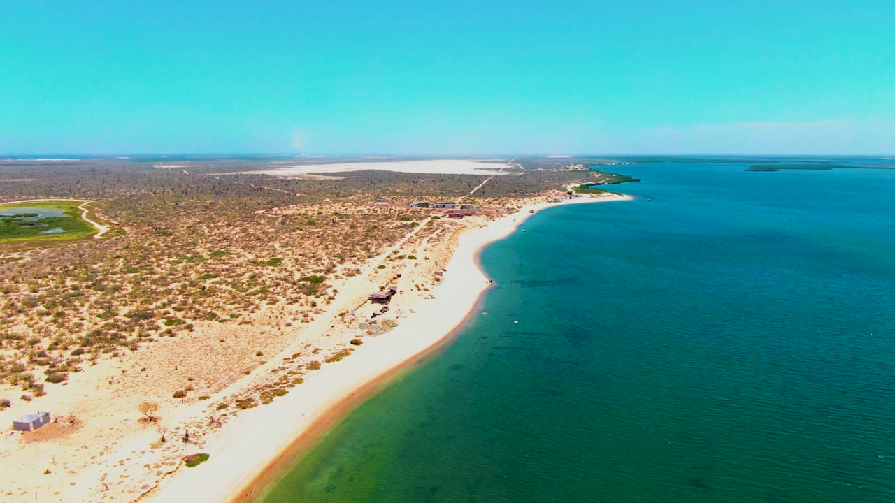 Curving sandy shoreline with turquoise shallows and dry land