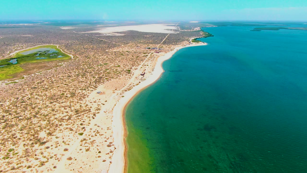 San Carlos, Baja California Sur shoreline from above, with the sandy coast bending around turquoise water, arid terrain on the left, distant shoreline across the top, and no visible people.