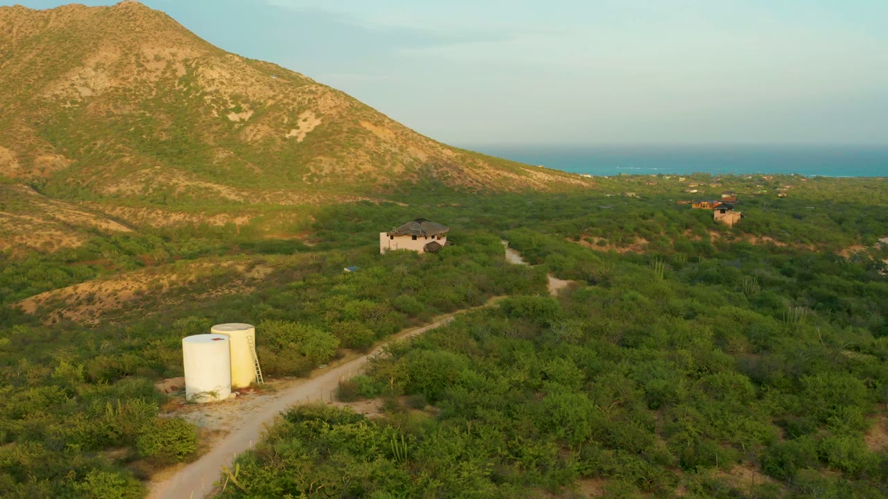 Aerial landscape with white tanks beside a dirt road and mountain rising behind green terrain.