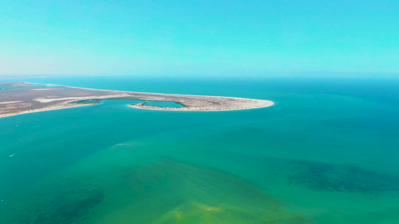 Aerial view in San Carlos, Baja California Sur, showing a pale sandy island across turquoise water with darker submerged patches and no visible people.