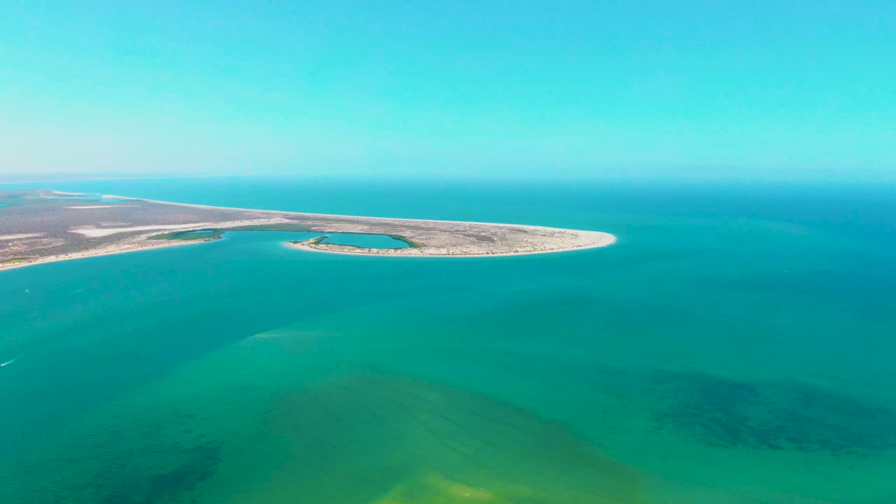 Aerial view over turquoise sea in San Carlos, Baja California Sur, with the sandy island stretching left to right near the horizon and no visible people.