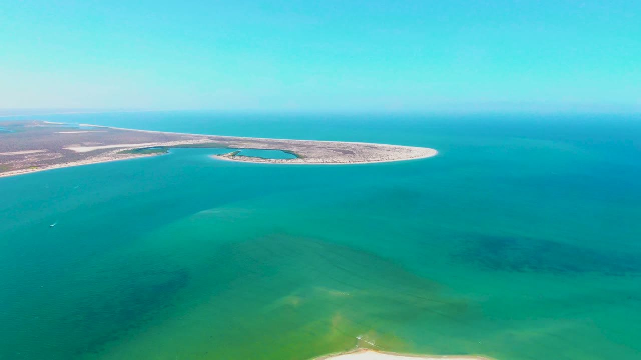 Aerial view over San Carlos, Baja California Sur, with a narrow pale sandbar across the midground, turquoise water in front, open sea beyond, and no visible people.
