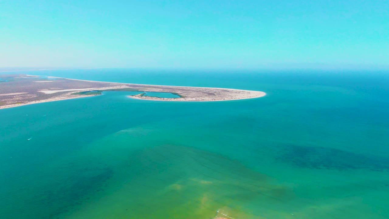 Wide drone view of a sandbar with shallow blue-green water in the foreground.