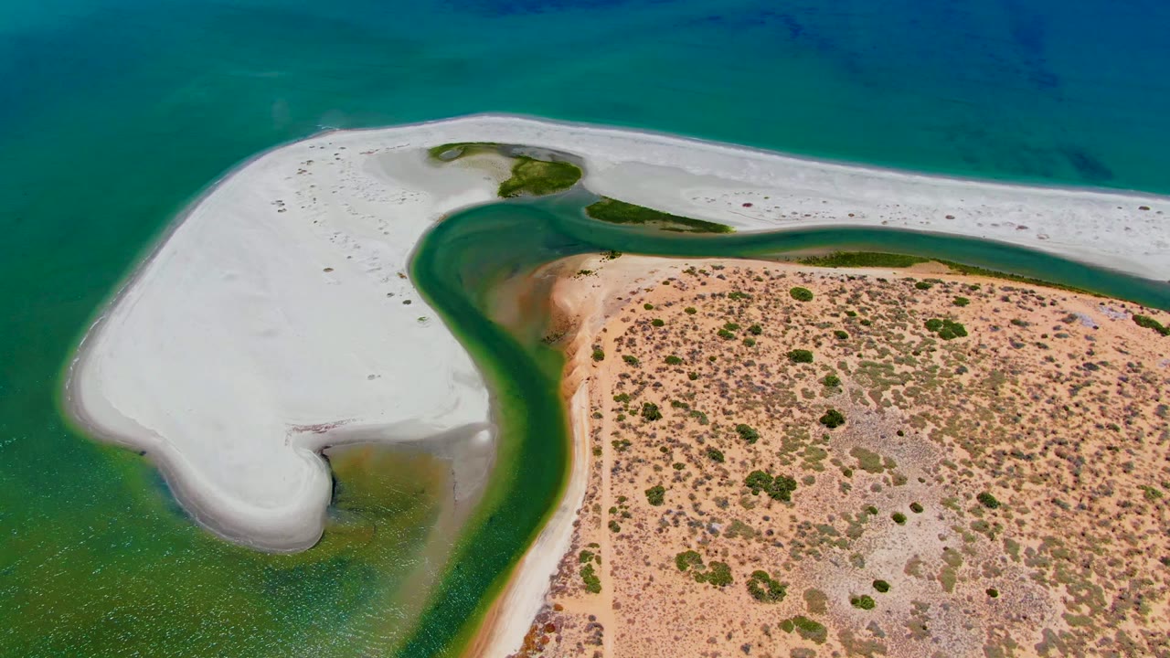 Opening aerial frame over San Carlos, Baja California Sur showing a white sandbar, curved green channel, tan scrub-covered shoreline, turquoise water, and no visible people.