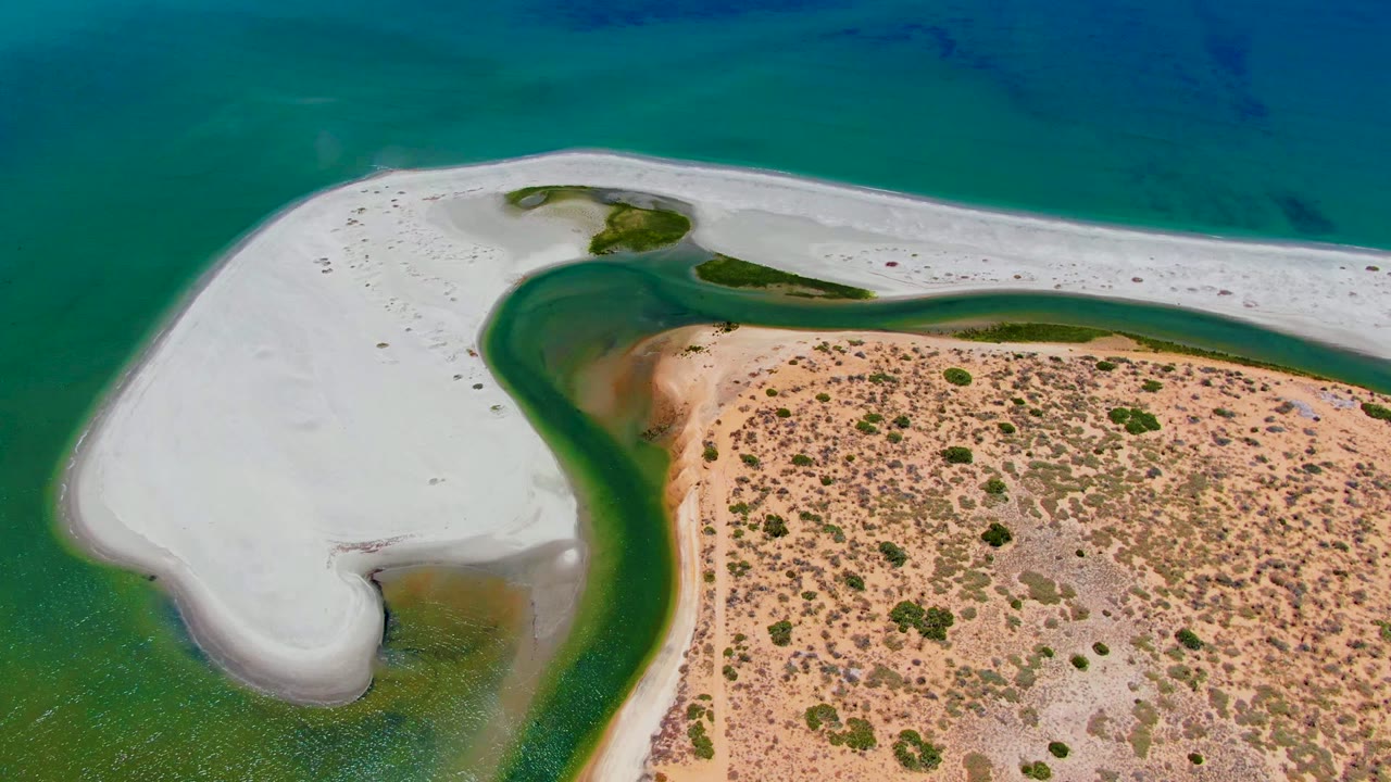 White sand spit curves around a green channel beside dry sandy terrain.