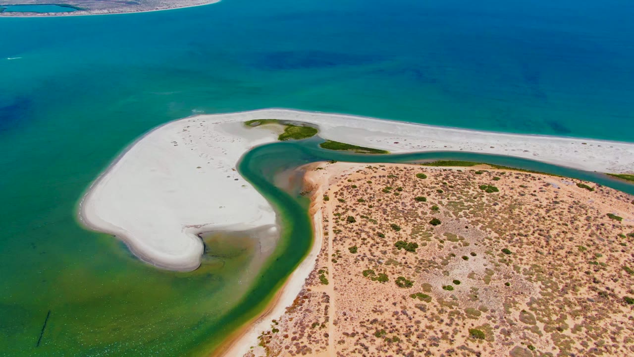 Overhead view in San Carlos, Baja California Sur, where the white sandbar stretches across the frame between turquoise offshore water and tan scrubland, with no visible people.