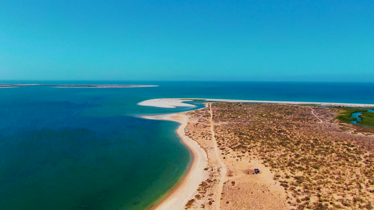 High aerial view of a dirt road crossing sandy beach terrain beside blue-green water.