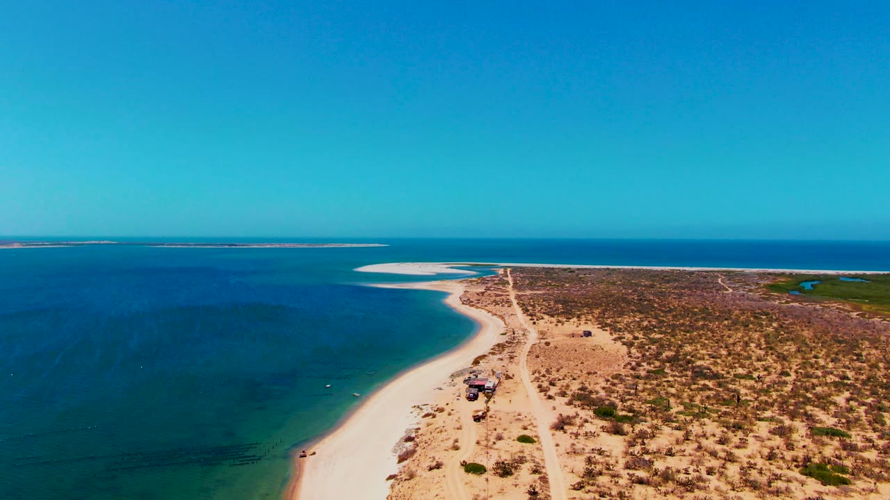 Vehicle on a coastal dirt road beside clear blue water and dry scrub.