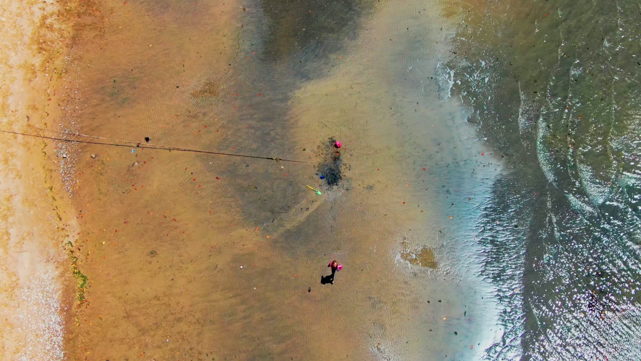 Aerial view in San Carlos, Baja California Sur with the person in pink farther down the wet beach, reflective water to the right, and tan sand with darker tide marks to the left.