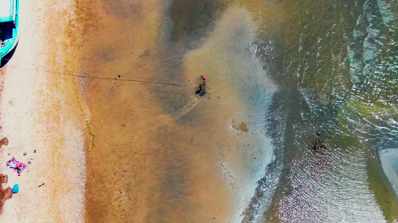 Overhead view of tan sand and rippled shallow water with people wading near the center.