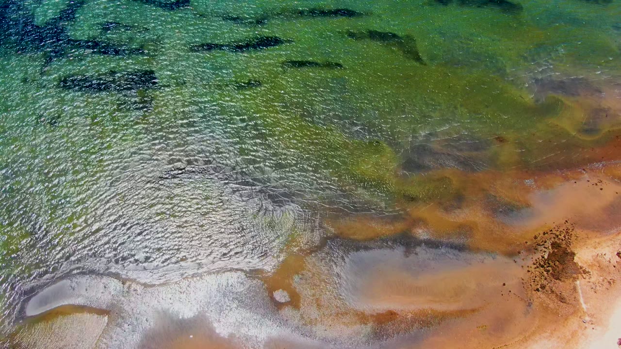 Aerial frame from San Carlos, Baja California Sur, Mexico showing pale wet sand under clear water, brown tidal shapes, darker submerged patches, and no visible people.