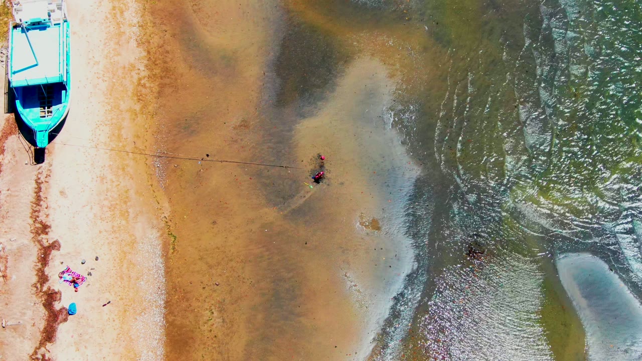 Blue boat, towels, and people in shallow water seen from above.