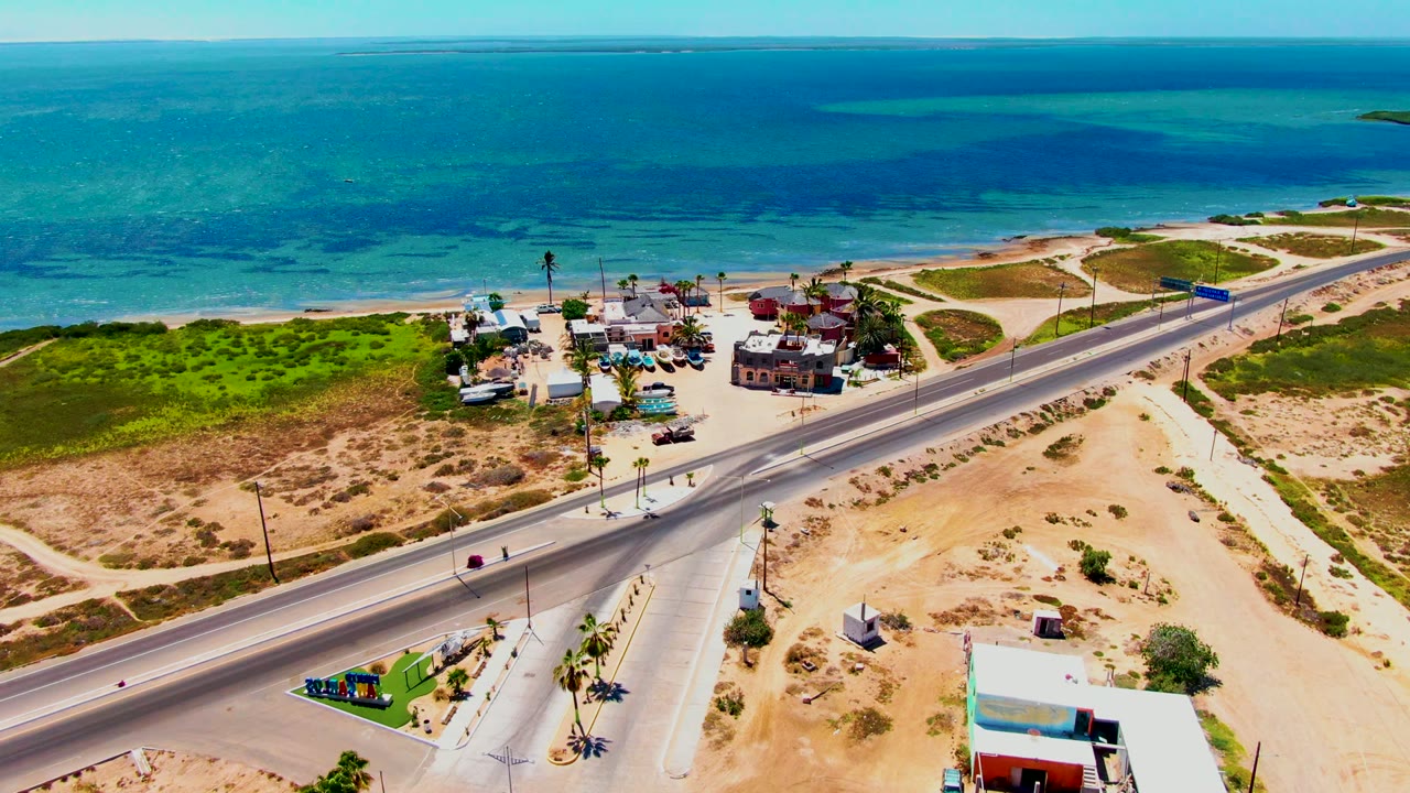 Drone view of road traffic near sandy shoreline and low coastal buildings.