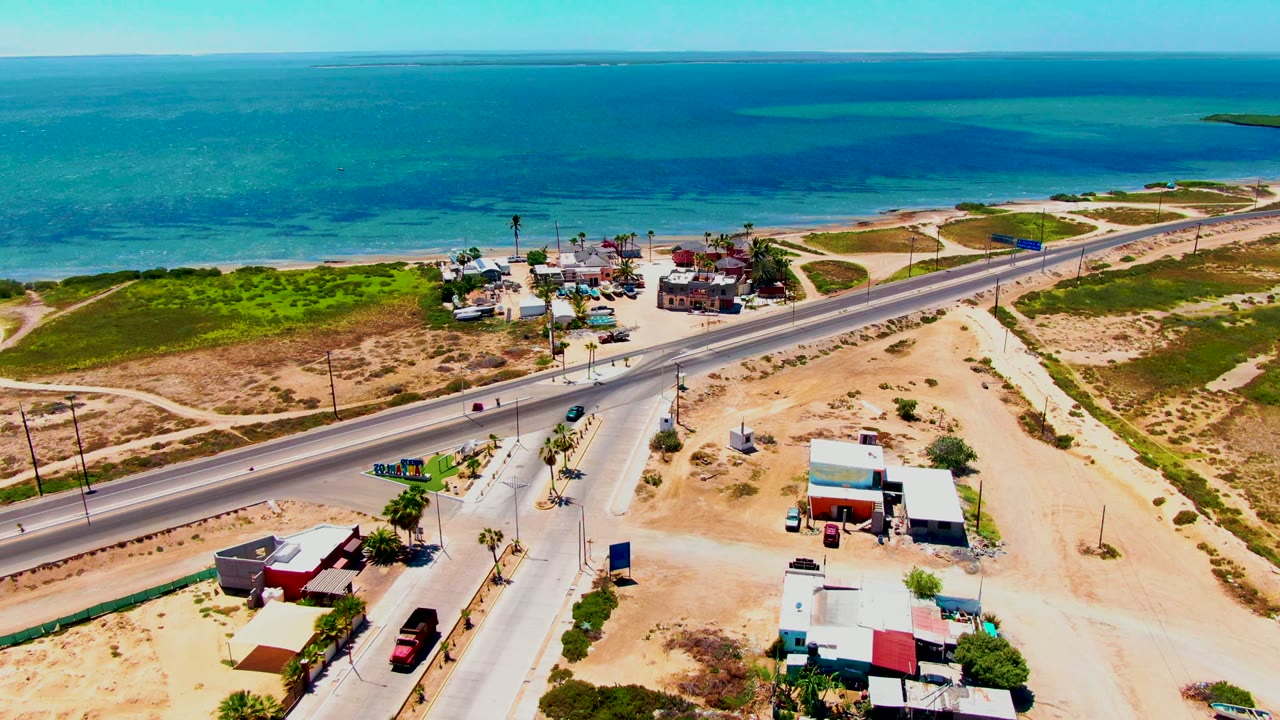 Drone view of vehicles on a road near low buildings and the shoreline