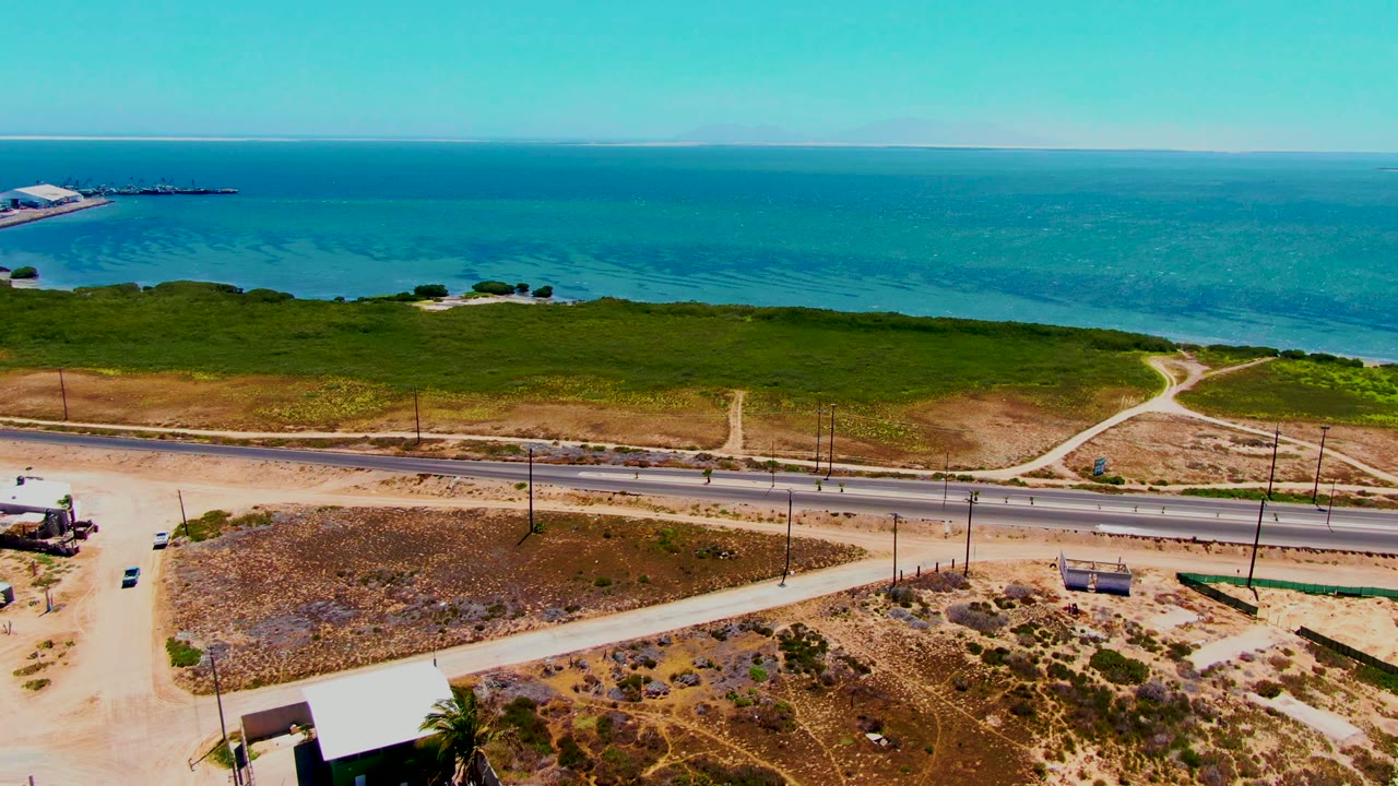 Coastal highway with vehicles, dirt paths, scrubland, and ocean horizon.