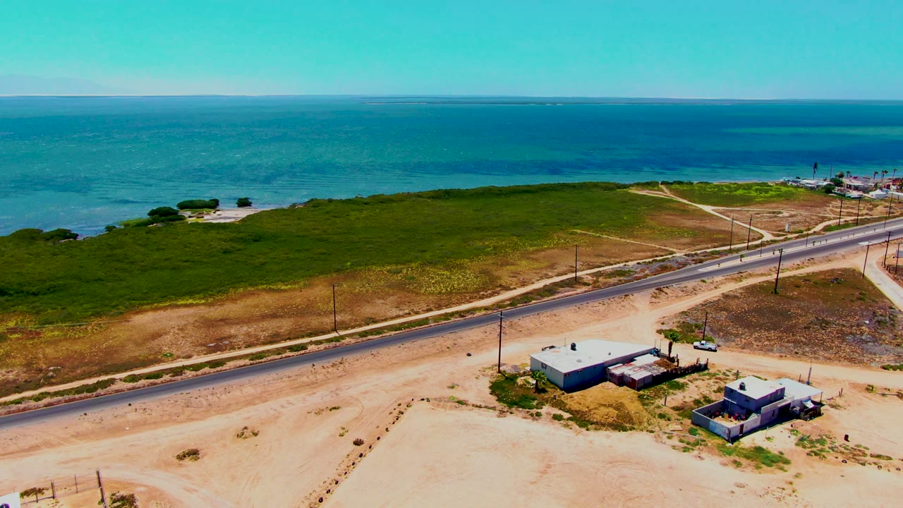 Coastal highway crossing sandy terrain with ocean and scrubland beyond.
