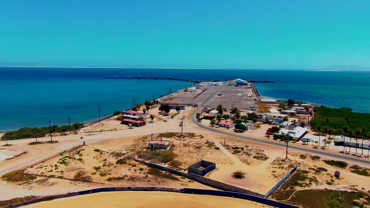 High coastal view with a road crossing sandy terrain beside blue water.