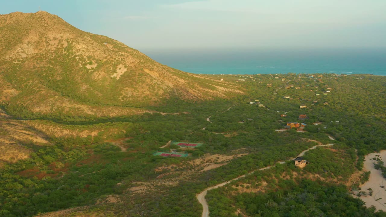 At two seconds, the Cabo Pulmo frame shows the rocky mountain and green valley with an orange-roofed cluster near center right, curving dirt roads below, the ocean beyond, and no visible people.