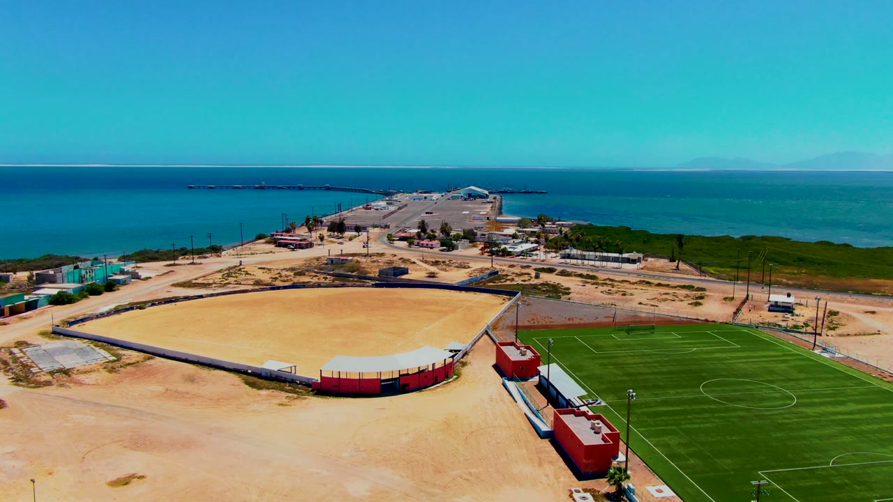 Drone view of a sandy arena, soccer field edge, pier, and open sea.
