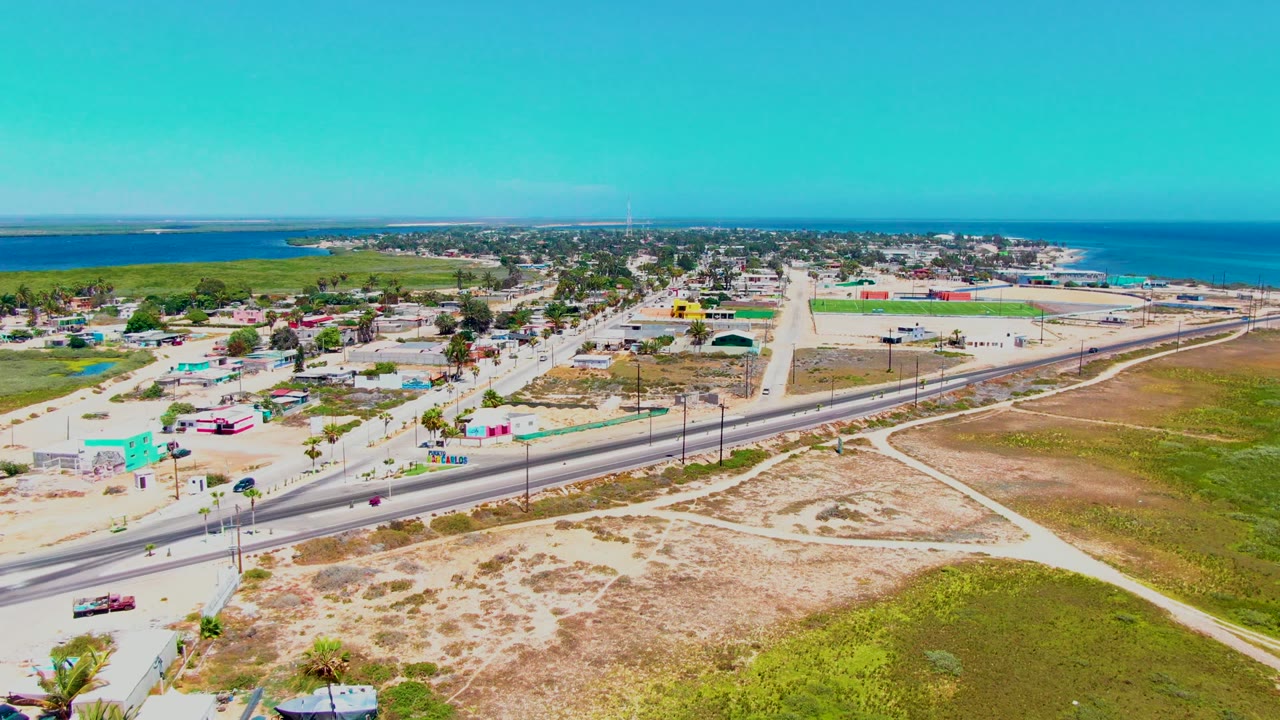 Drone view of highway traffic beside dry land, small town buildings, and ocean.