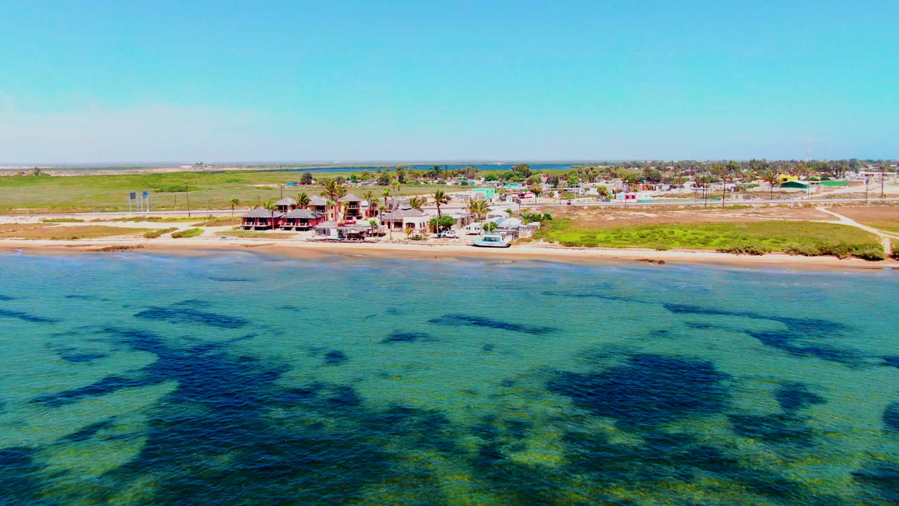 Shallow blue-green ocean beside a sandy shore with beachfront buildings.