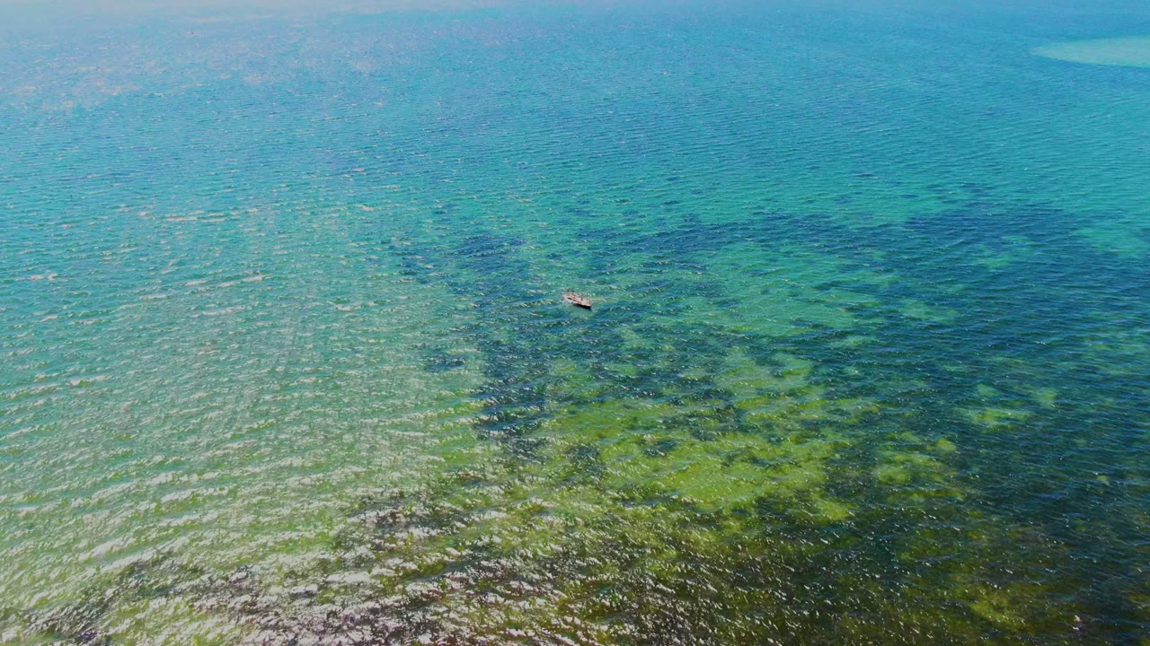 Clear blue-green water with seabed texture and a small boat farther across the frame.