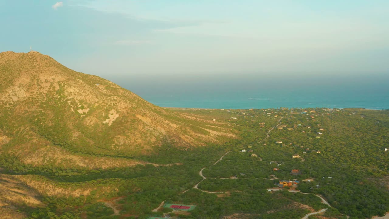 Aerial mountain slope above green valley with coastline in background