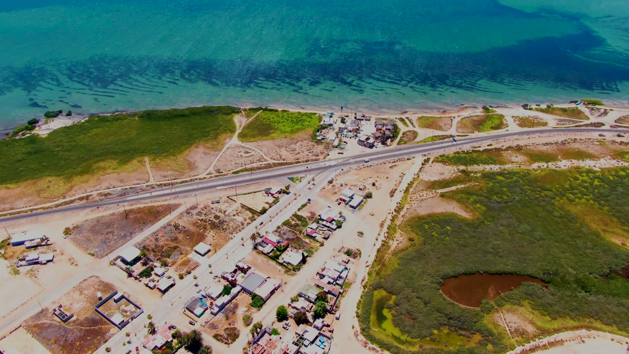 Overhead view of traffic on a road between ocean and low buildings.