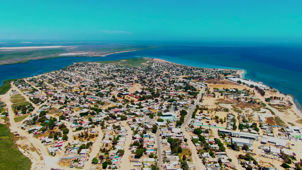 Drone view of a coastal neighborhood beside turquoise water and open ocean.
