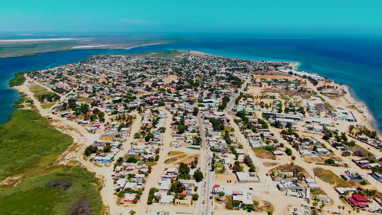 Wide drone view of sandy streets and homes beside coastal water
