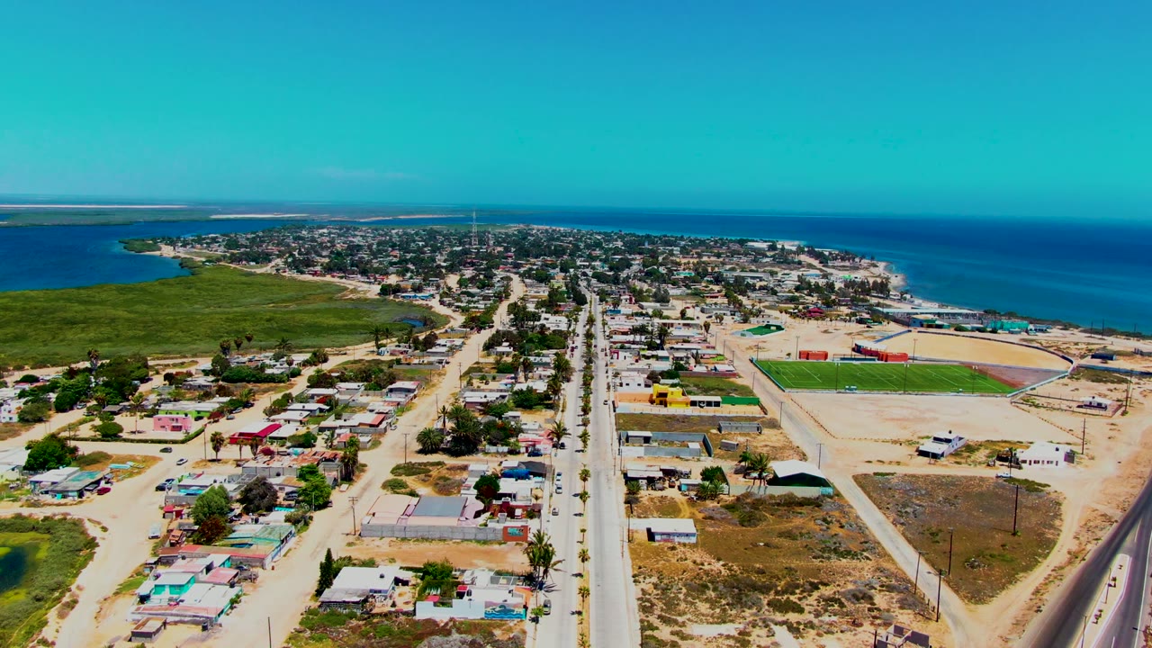 Drone view of a straight road through houses near the ocean.