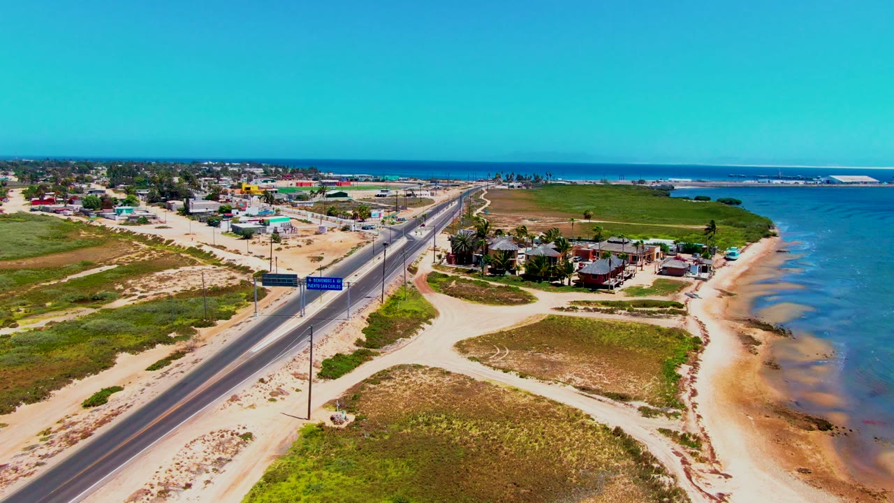 Coastal highway with vehicles, road signs, beach, and ocean from above.