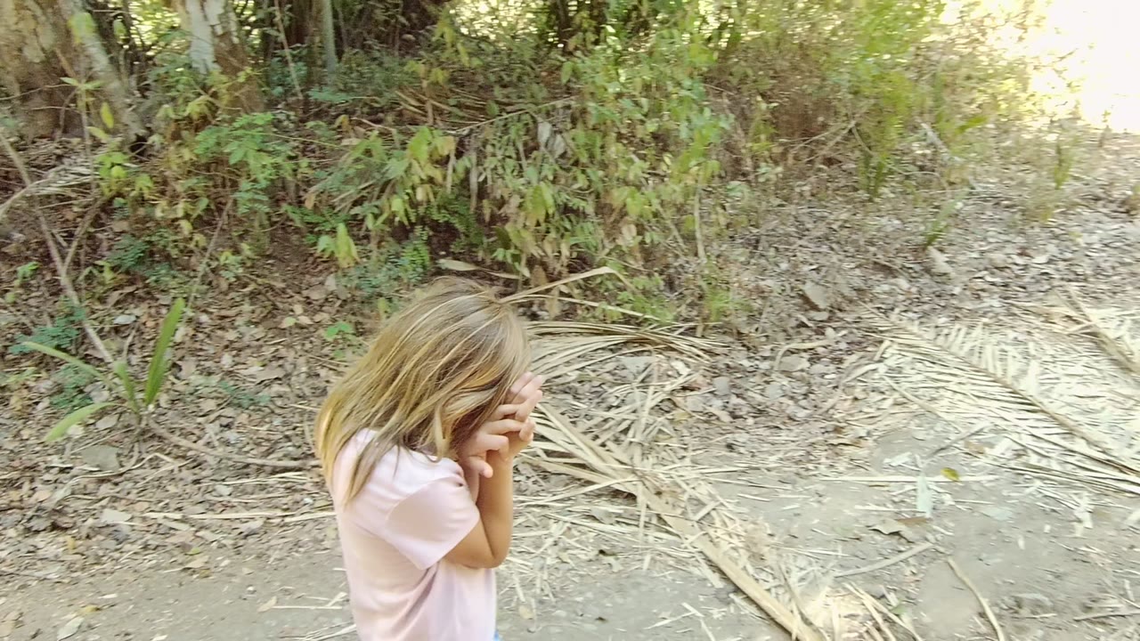 Girl stands near dry leaves and brush with hands by her face.