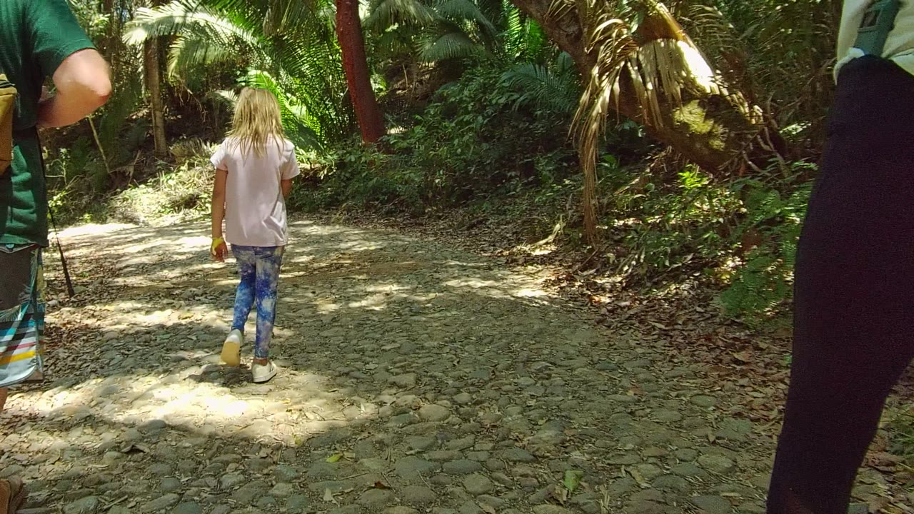 Child walking ahead on a sunlit rocky trail with an adult at the side.