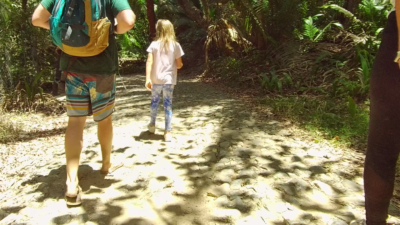 In San Pancho, Nayarit, Mexico, the child walks ahead near the center of the trail while an adult with a backpack remains in the foreground and another person appears at the right edge.
