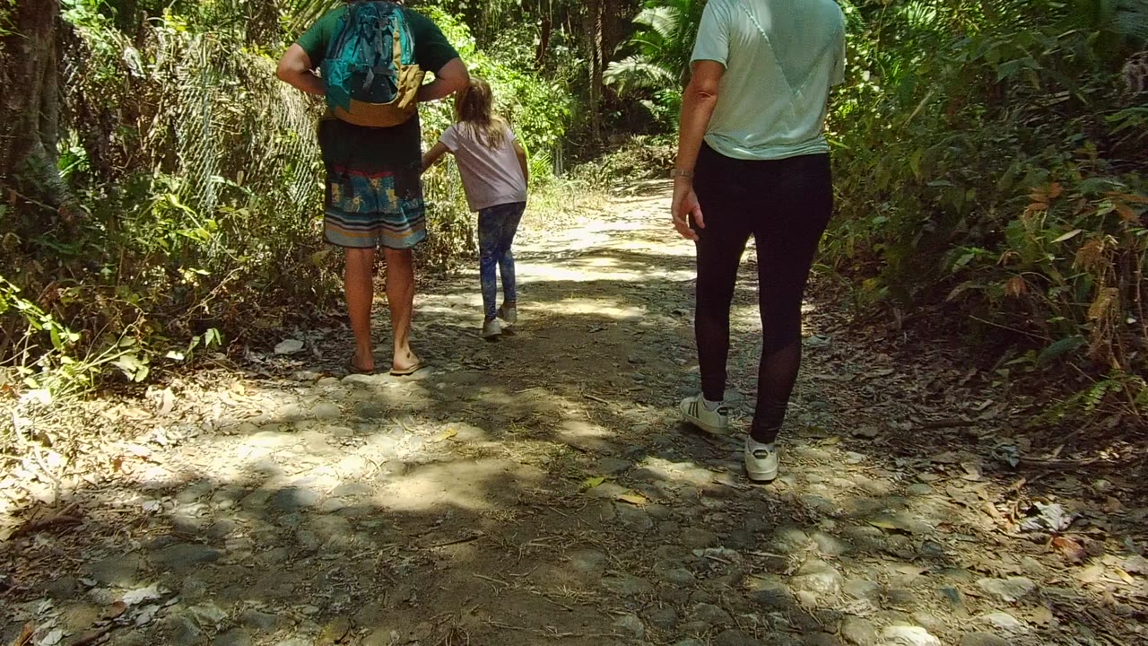 At 0:00, three people walk away on a dirt forest trail in San Pancho, Nayarit, Mexico, with the child near the center and adults on either side.