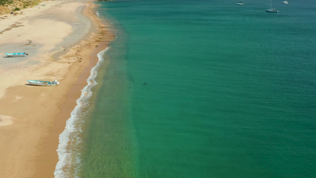 Aerial view in Los Frailes, Los Cabos, Baja California Sur showing turquoise water along a sandy beach, with small boats on the sand and offshore near the top of frame.