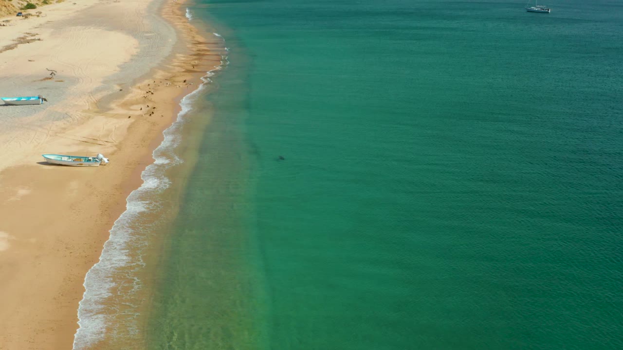 Sandy shoreline and turquoise water with small boats and distant beach activity.
