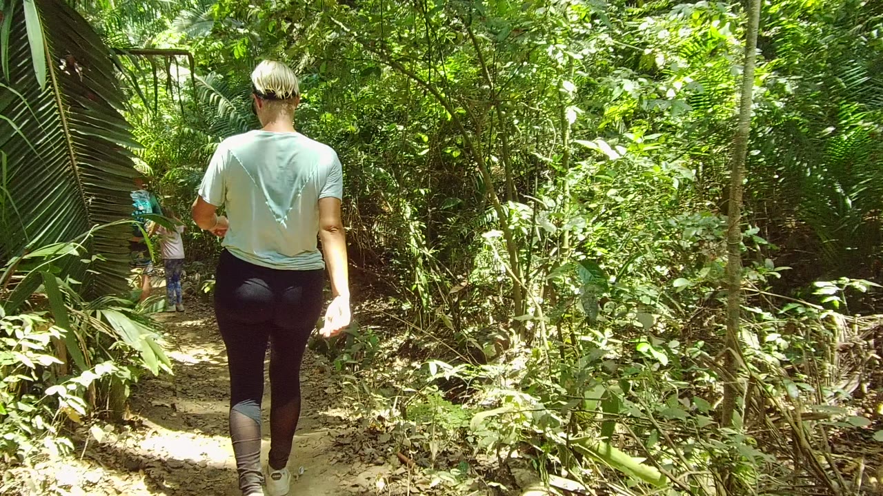In San Pancho, Nayarit, the foreground person walks away from camera while a second person with a backpack appears ahead on the winding forest trail.