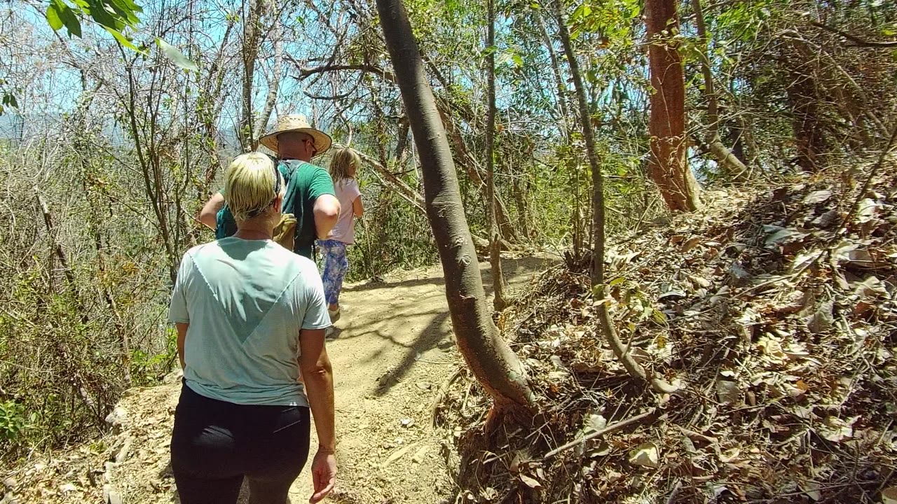 Two adults and a child move away on the San Pancho trail, with a backpacked hiker ahead and dry brush filling the sides of the frame.