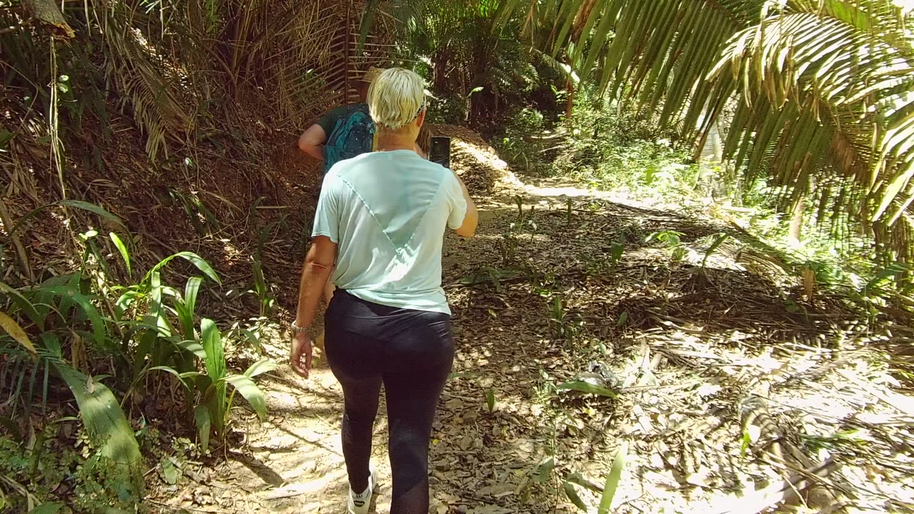 Adult follows another person along a leafy dirt path.