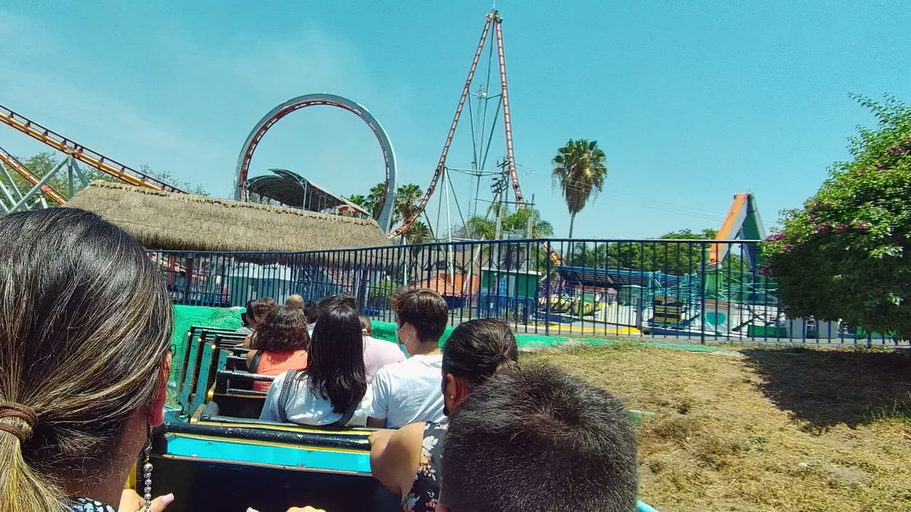 Ride passengers facing a thatched-roof structure and coaster loop
