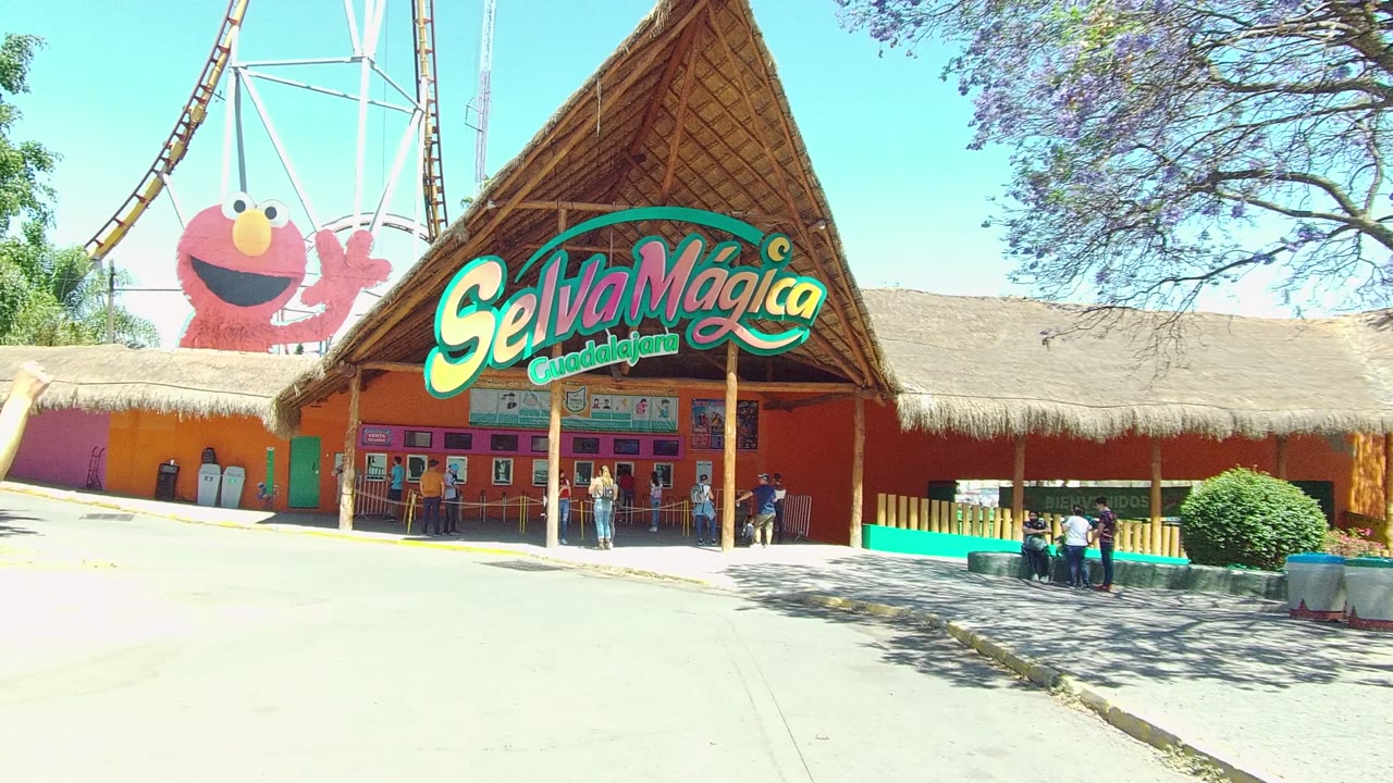 Theme park entrance with large Selva Magica sign, trees, and people by the ticket area.
